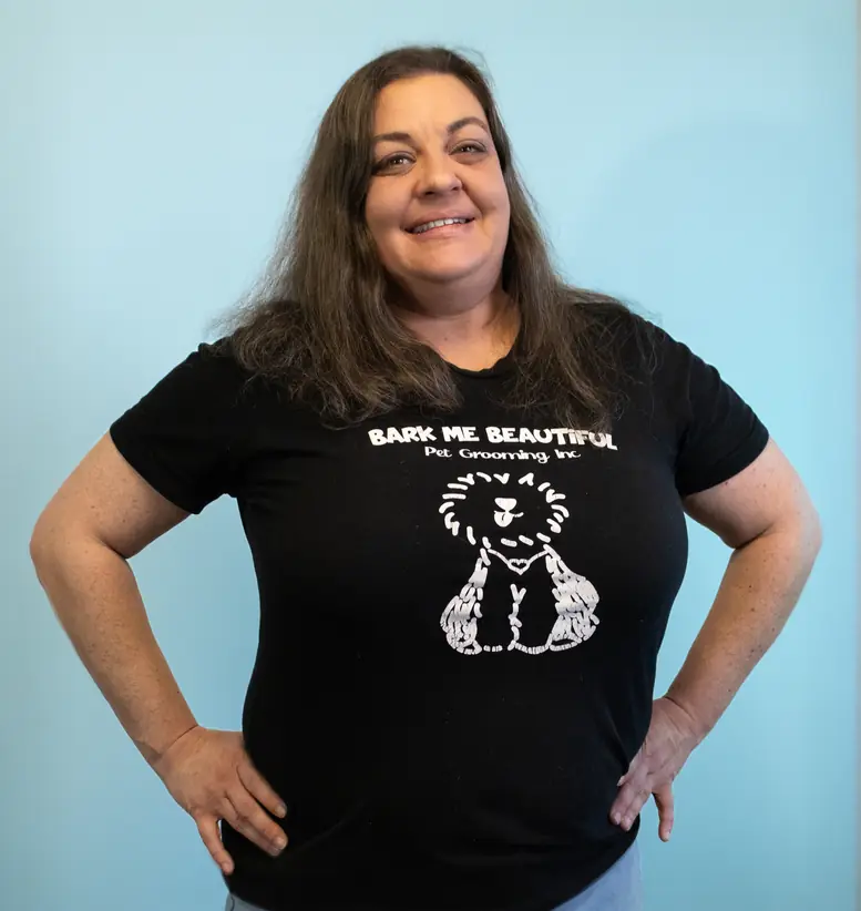 A team member in a black Bark Me Beautiful tee, hands on hips, in front of the turquoise wall